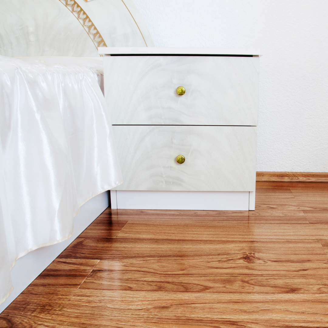 A bedroom with a wooden floor and a white nightstand