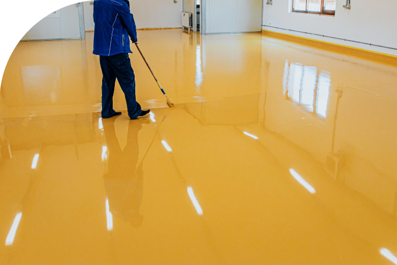 A man applying self-leveling epoxy on a yellow floor in a warehouse.