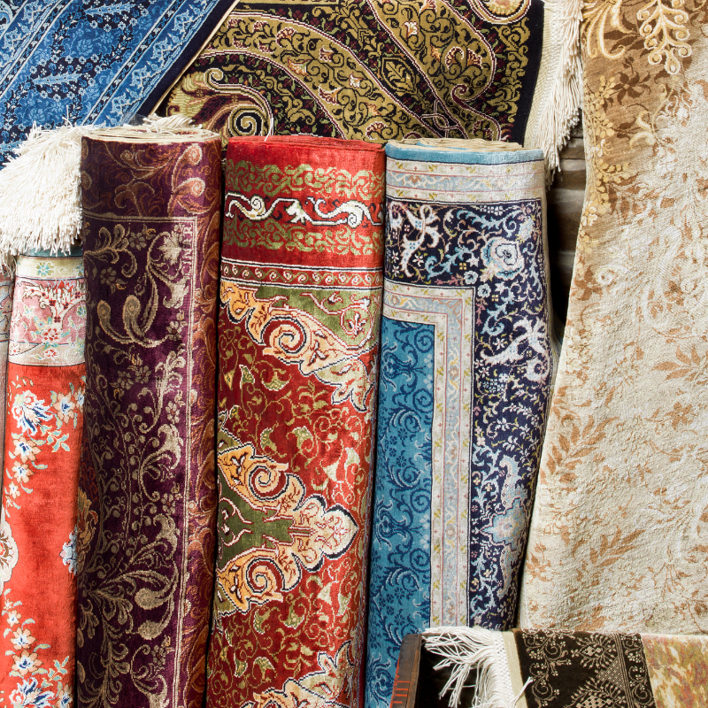 A bunch of colorful silk rugs are stacked on top of each other