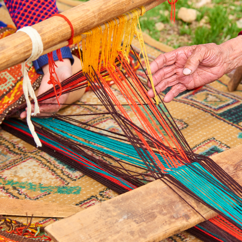 A person is using a loom to weave a rug