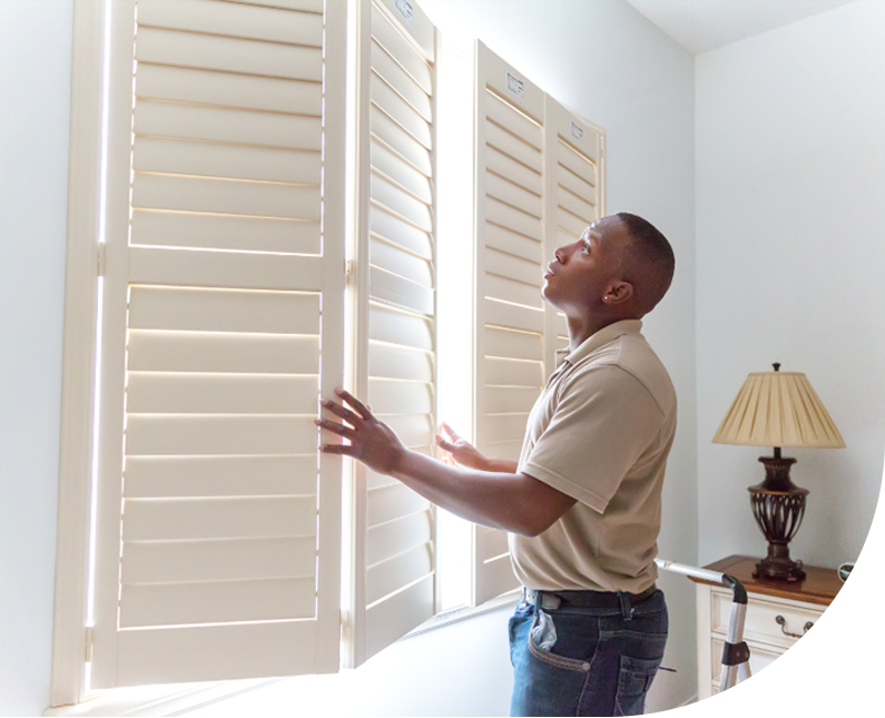 window treatment installer installing wooden shutters in a residential home