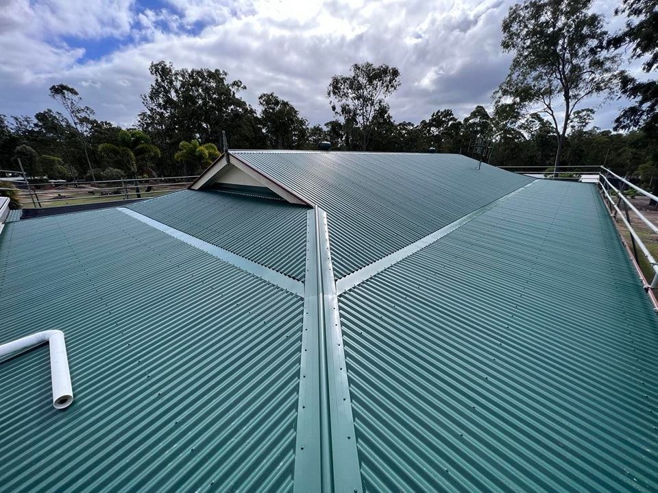Green Corrugated Metal Roof With Light Sky and Trees in Background — Venom Roofing Pty Ltd in Landsborough, QLD