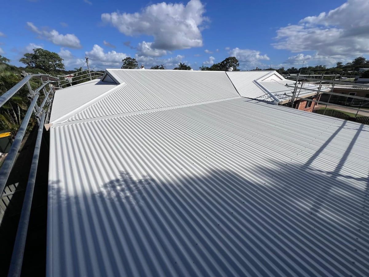 White Corrugated Metal Roof on a Building Under a Blue Sky With Clouds — Venom Roofing Pty Ltd in Sunshine Coast, QLD