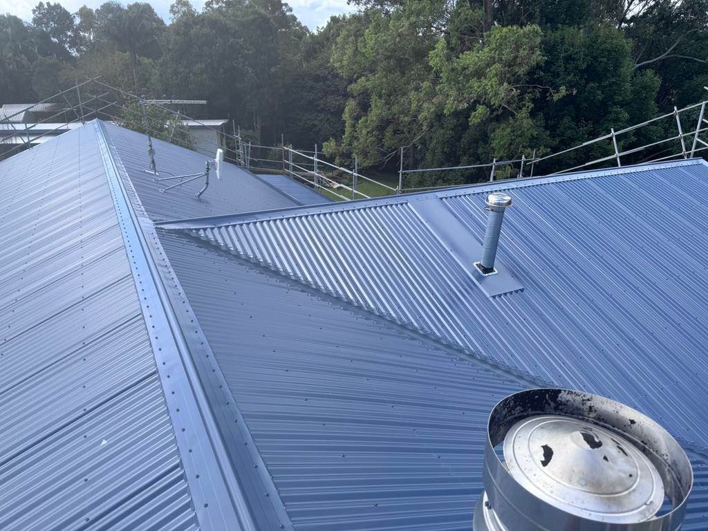 Blue Corrugated Metal Roof With Chimneys and Trees in the Background — Venom Roofing Pty Ltd in Sunshine Coast, QLD
