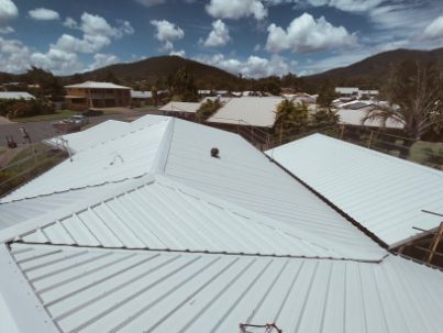 White Metal Roofs of Buildings With Mountain Backdrop Under a Cloudy Sky — Venom Roofing Pty Ltd in Sunshine Coast, QLD