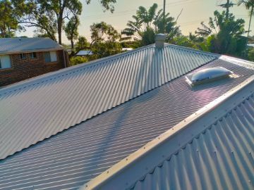 Corrugated Metal Roof With a Skylight, Chimney, and a Home in the Background  — Venom Roofing Pty Ltd in Sunshine Coast, QLD