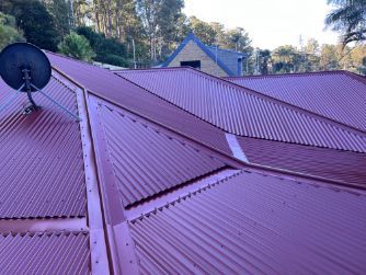 Red Metal Roof With Satellite Dish, Set Against Backdrop of Trees and a House — Venom Roofing Pty Ltd in Sunshine Coast, QLD