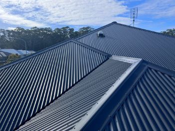 Dark Corrugated Metal Roof With a Blue Sky and Trees in the Background — Venom Roofing Pty Ltd in Sunshine Coast, QLD