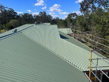 Green Metal Roof Under a Blue Sky With Safety Scaffolding Surrounding Trees — Venom Roofing Pty Ltd in Sunshine Coast, QLD