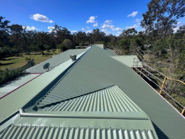 Green Metal Roof With Multiple Sections Against a Background of Trees — Venom Roofing Pty Ltd in Sunshine Coast, QLD