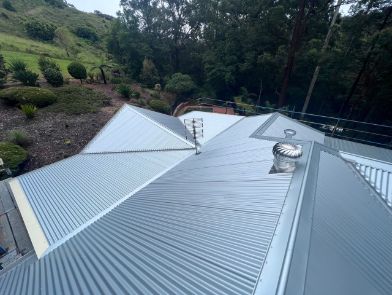 Grey Corrugated Metal Roof on a House, Set Against a Hillside With Trees — Venom Roofing Pty Ltd in Sunshine Coast, QLD