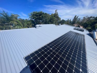 Solar Panels on a Gray Corrugated Metal Roof Under a Bright Blue Sky — Venom Roofing Pty Ltd in Sunshine Coast, QLD