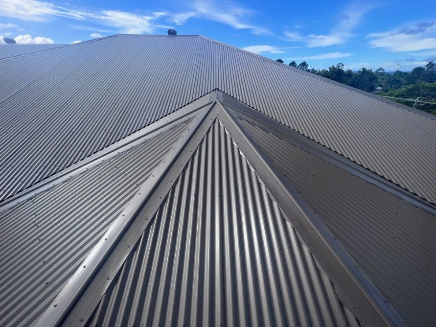 Gray Corrugated Metal Roof With a Triangular Design Against a Bright Blue Sky — Venom Roofing Pty Ltd in Sunshine Coast, QLD