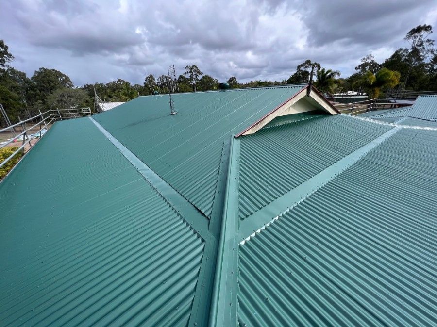 Green Corrugated Metal Roof on a Building Against a Cloudy Sky — Venom Roofing Pty Ltd in Sunshine Coast, QLD
