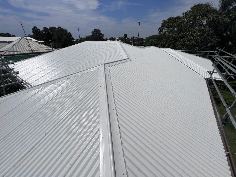 White Corrugated Metal Roof on a Building Against a Blue Sky With Trees — Venom Roofing Pty Ltd in Sunshine Coast, QLD