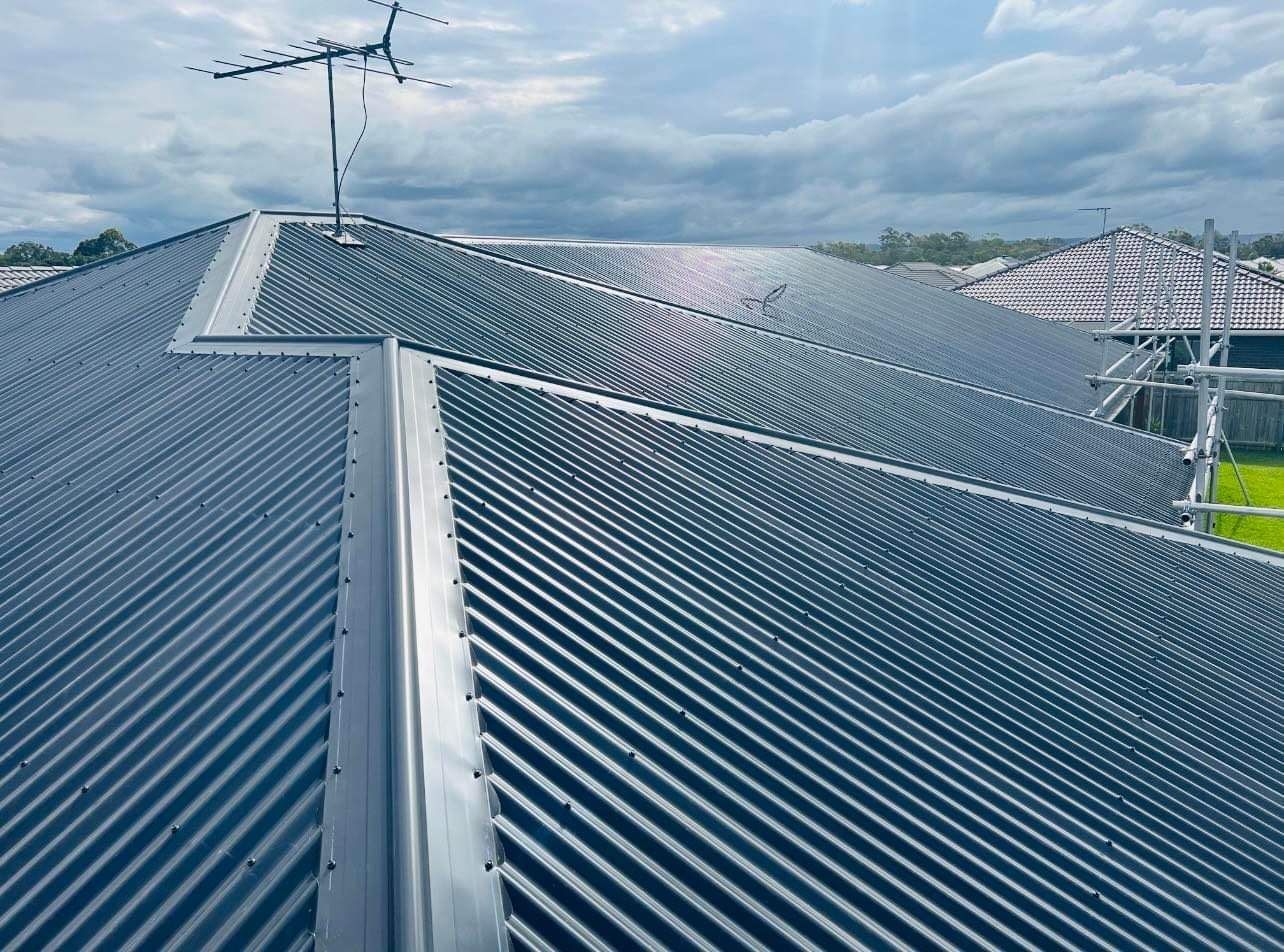 Gray Corrugated Metal Roof With an Antenna, on a House Under a Cloudy Sky — Venom Roofing Pty Ltd in Sunshine Coast, QLD