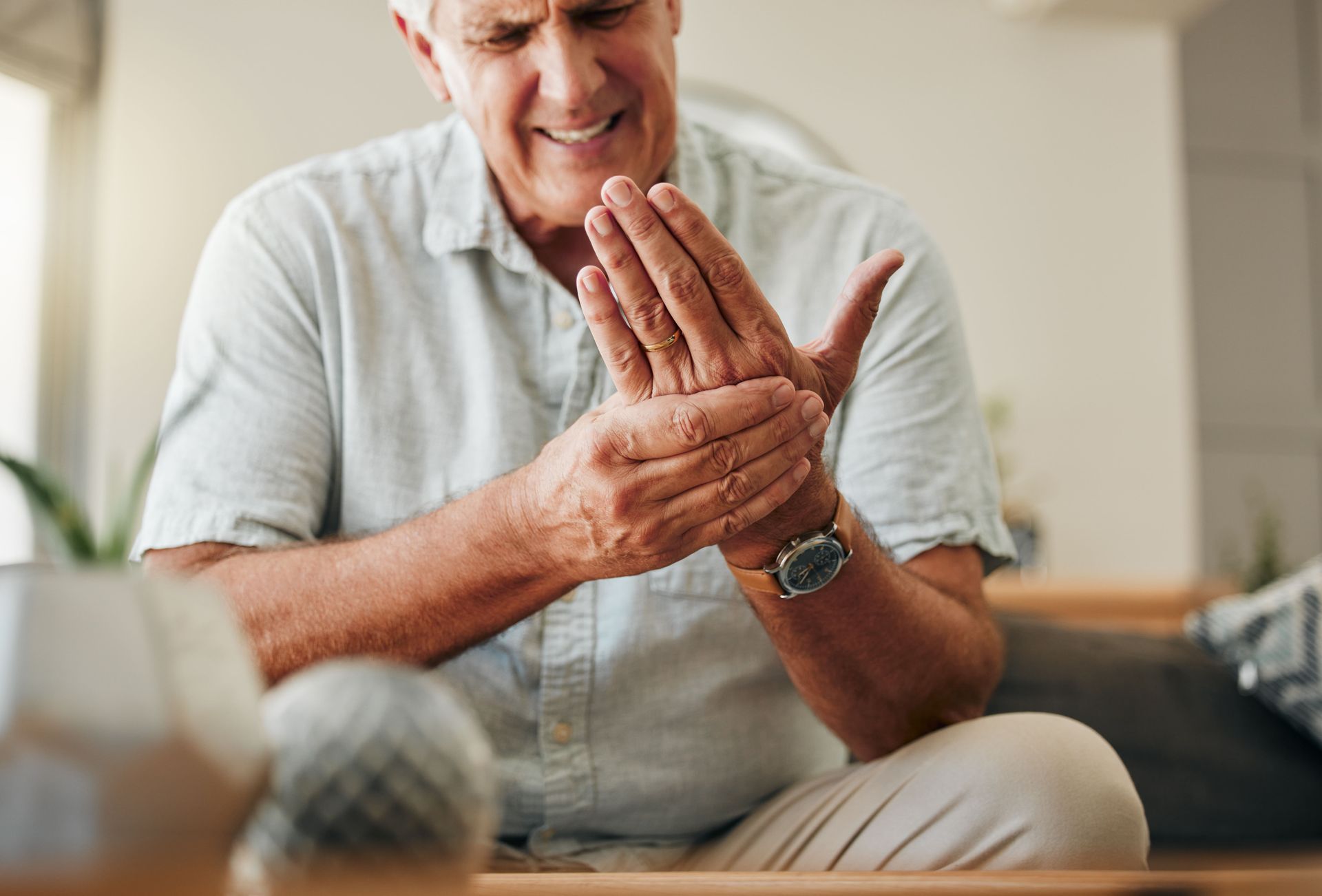 An elderly man is sitting on a couch holding his wrist in pain.