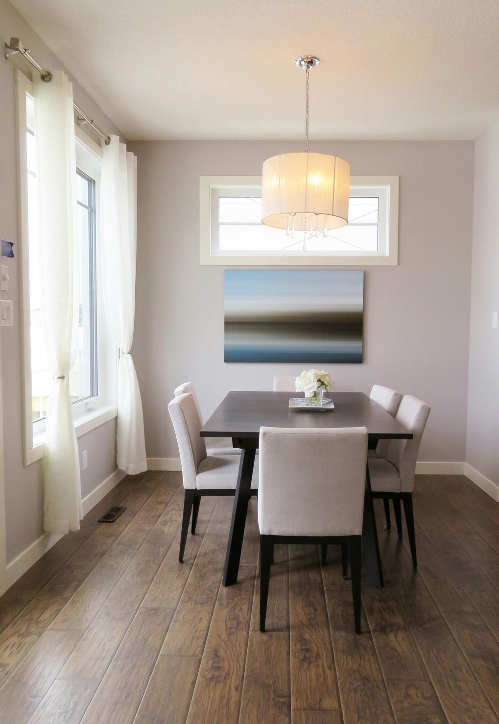 A dining room with a table and chairs and a painting on the wall.