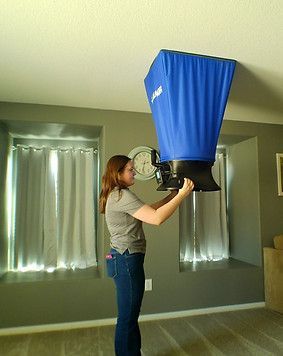 Woman installing a blue ceiling vent cover in a room with gray walls and curtains.