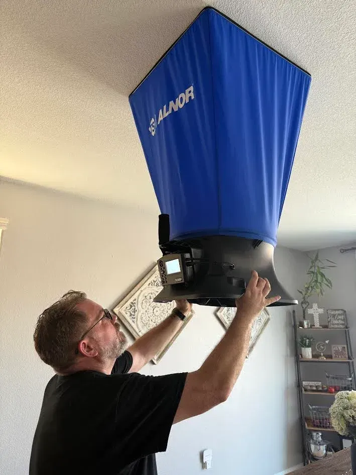 Man installing a blue, funnel-shaped device on a white ceiling. Device is labeled