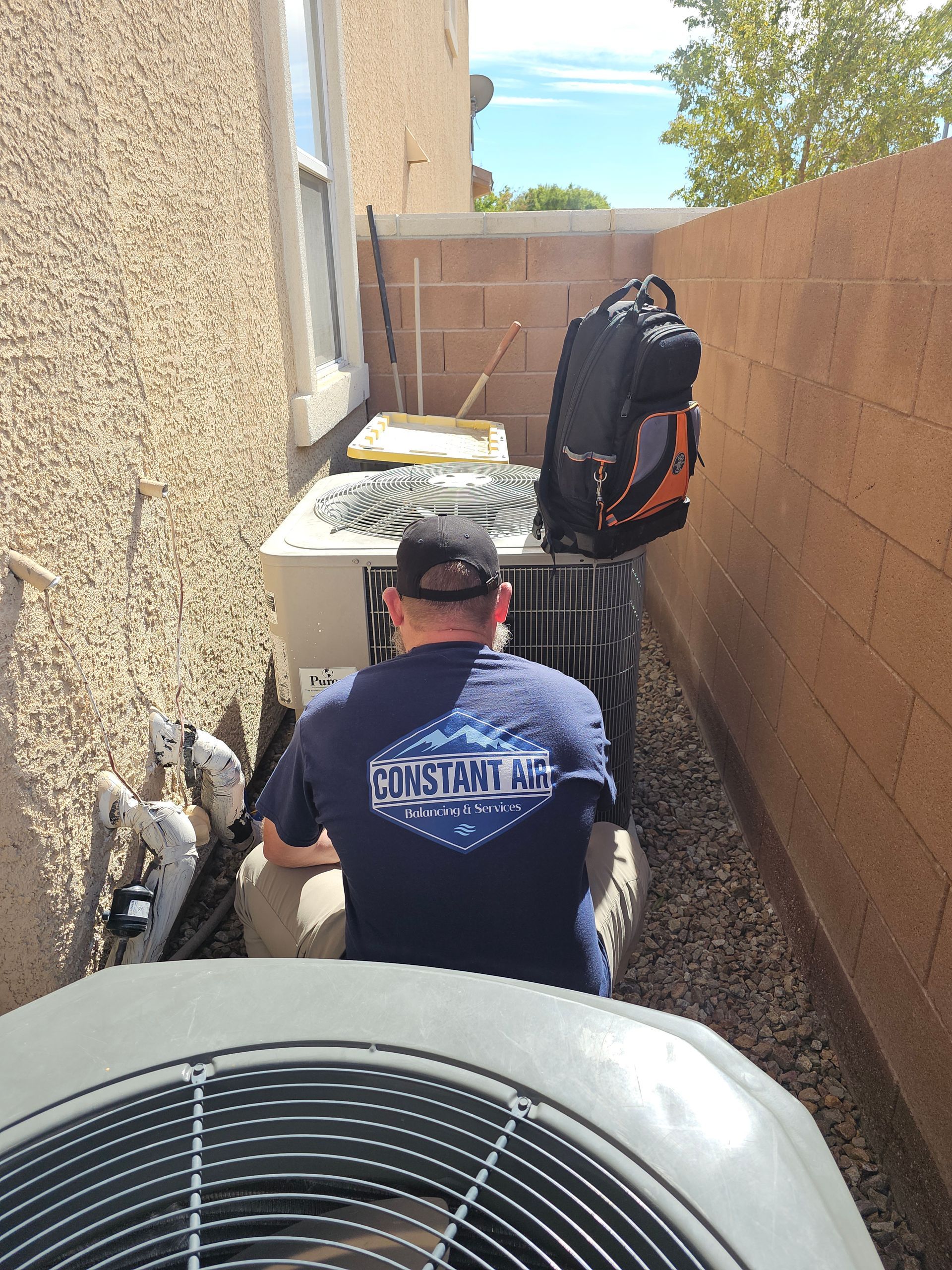 HVAC technician in a face mask, working on an outdoor air conditioning unit on a rooftop.