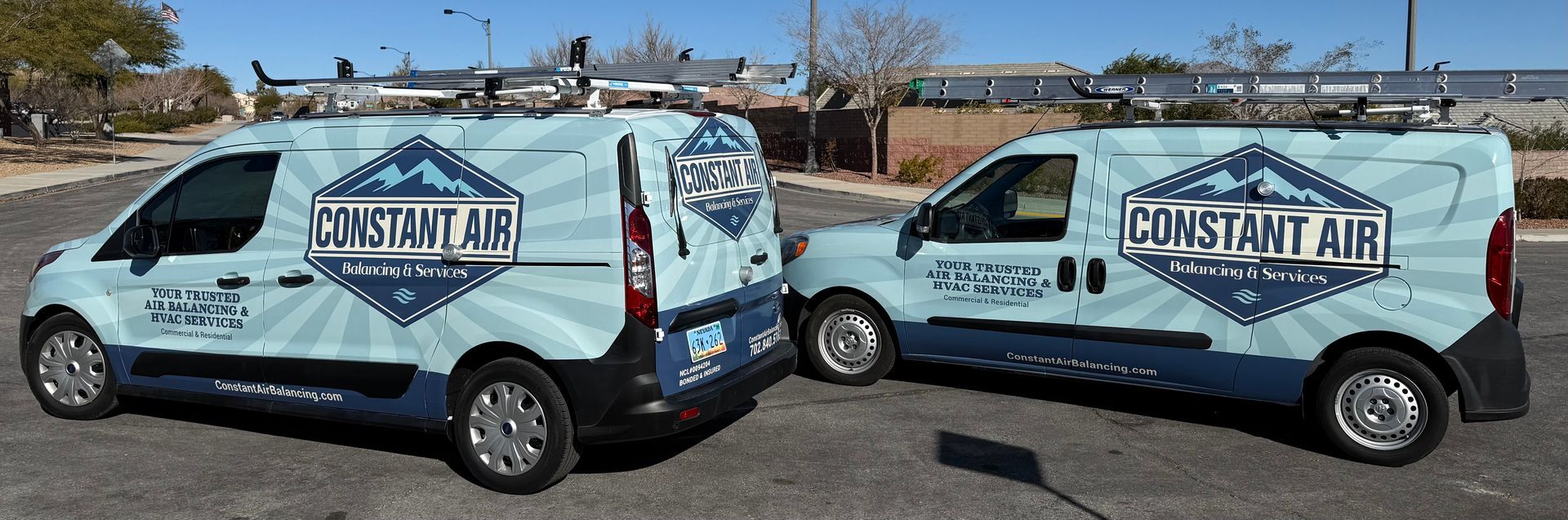 A white building with a flat roof. Two metallic boxes sit in front of the entrance. Black doors and a dark garage door are visible.