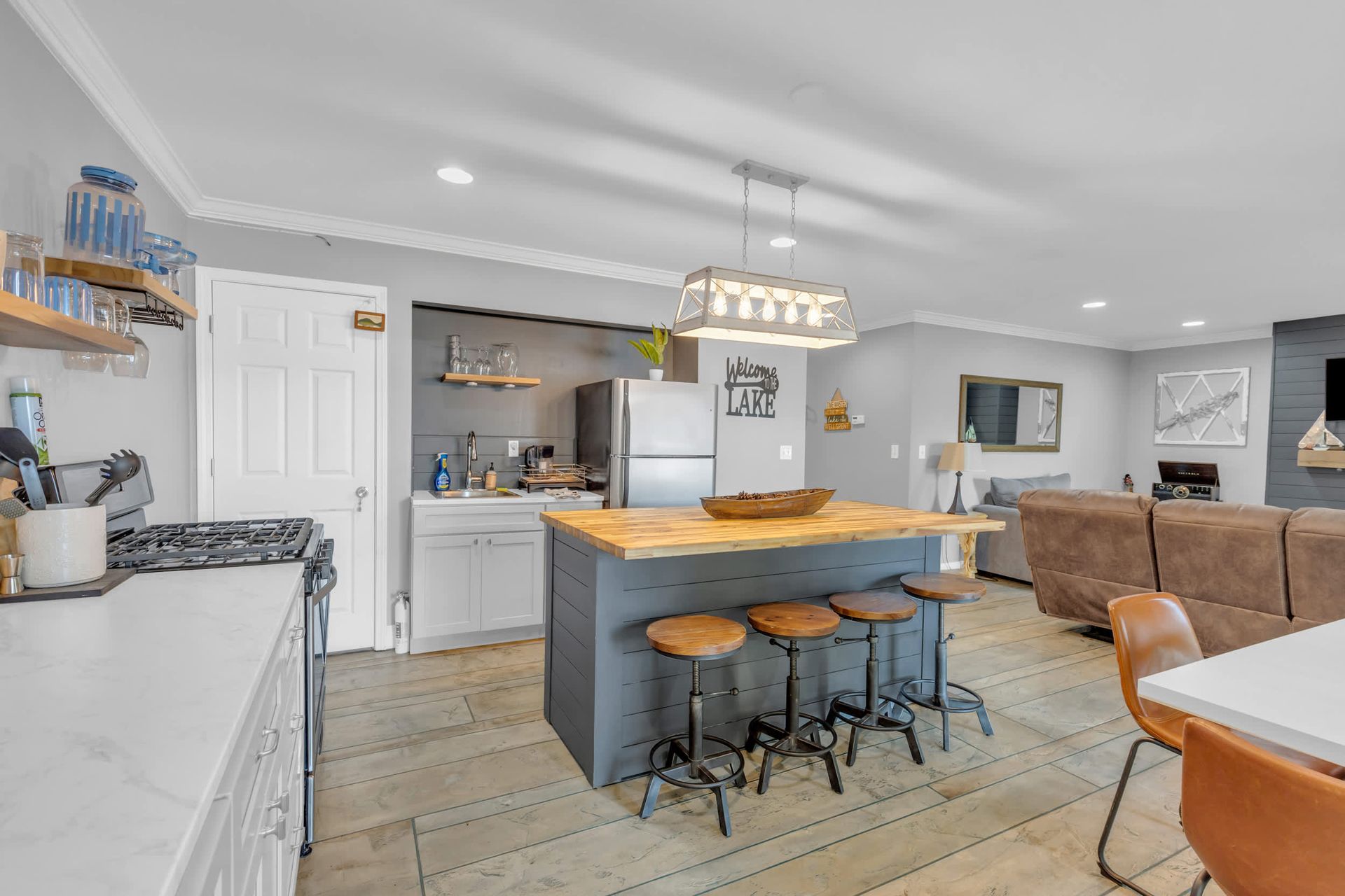 Open-concept kitchen with gray cabinets, a wood-top island with stools, and a living area with a brown sofa.