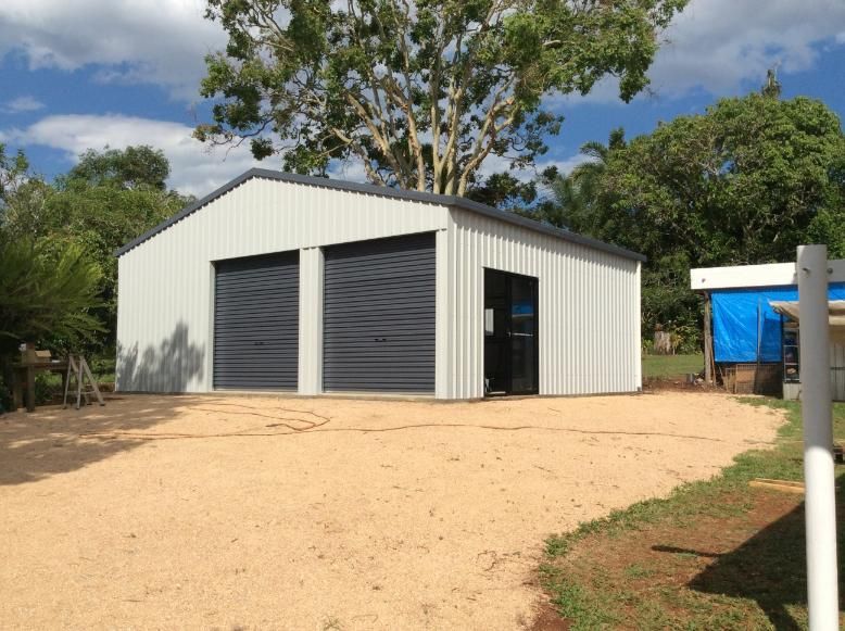 A Light Grey Metal Shed With Two Garage Doors and a Side Door Sits on a Gravel Driveway  — Bridgey's Constructions in Wallabi Point, NSW