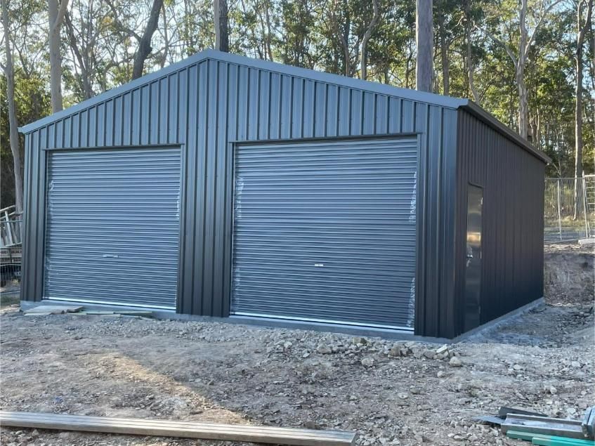Two-Car, Dark Grey Metal Garage in a Wooded Area With Two Roll-up Doors and a Side Door — Bridgey's Constructions in Pacific Palms, NSW