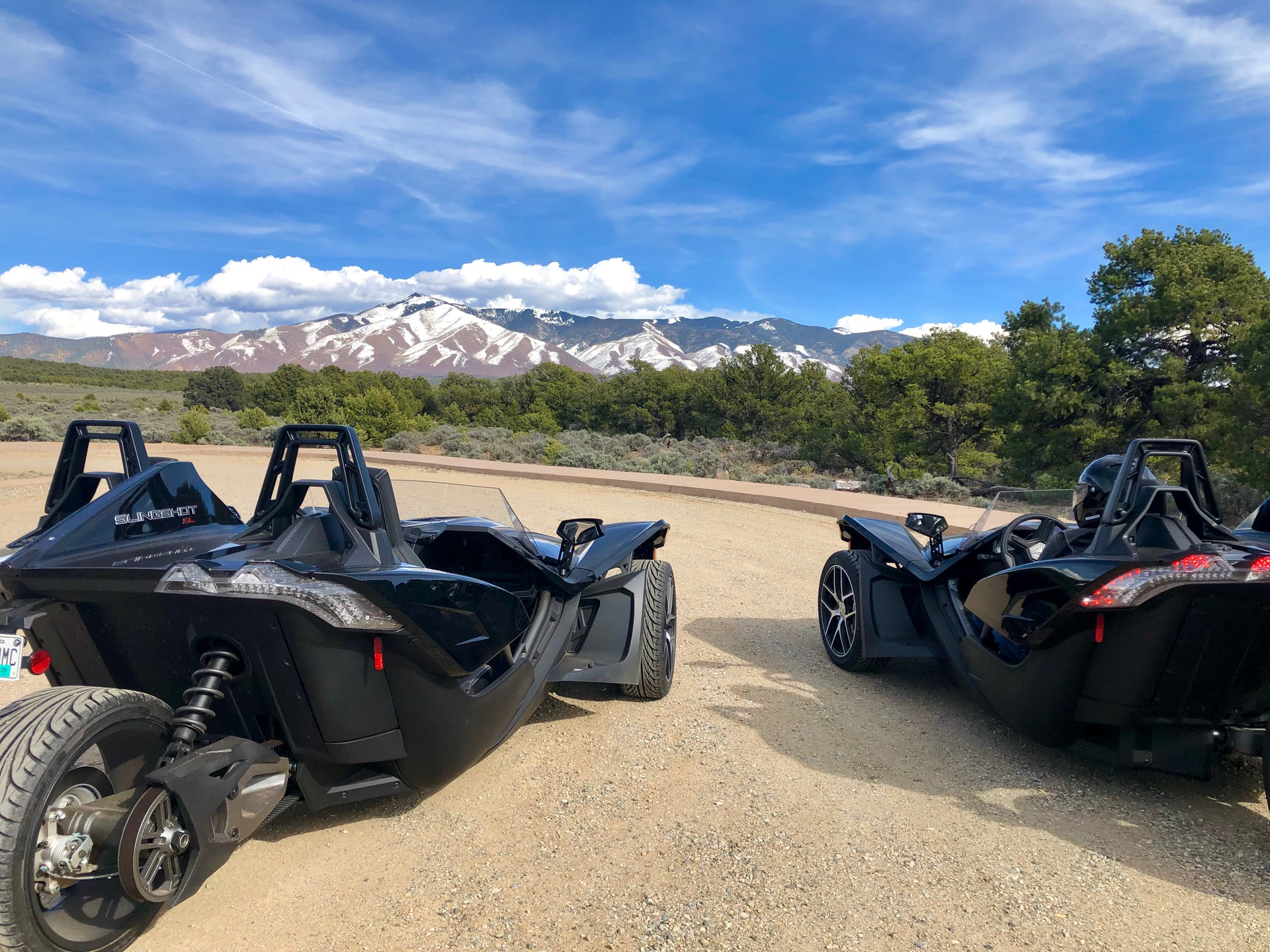 Two slingshot motorcycles are parked next to each other on a dirt road.