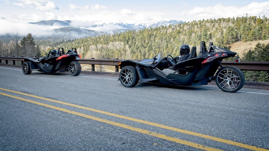 Two slingshot motorcycles are parked on the side of a road.