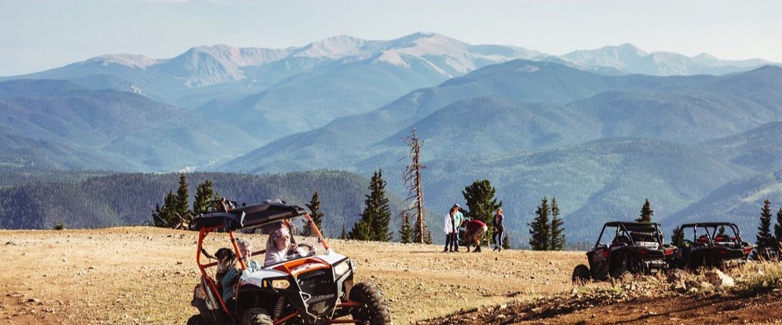 A group of people are riding atvs in a field with mountains in the background.