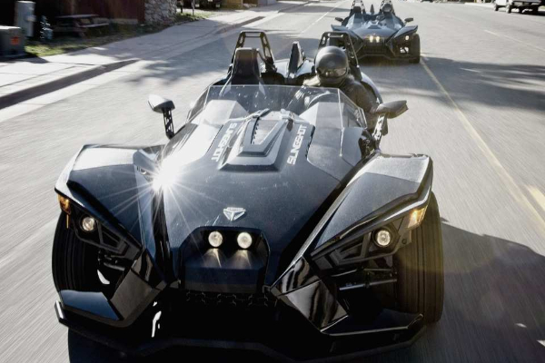 A black slingshot is driving down a street