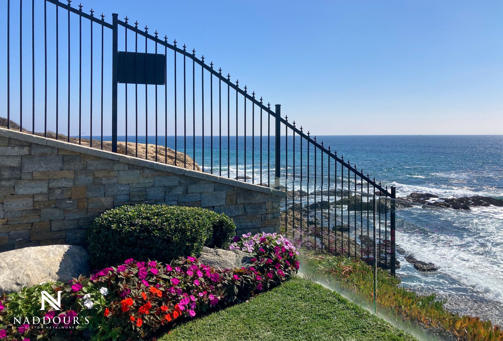 A wrought iron fence leading to the ocean with flowers in the foreground