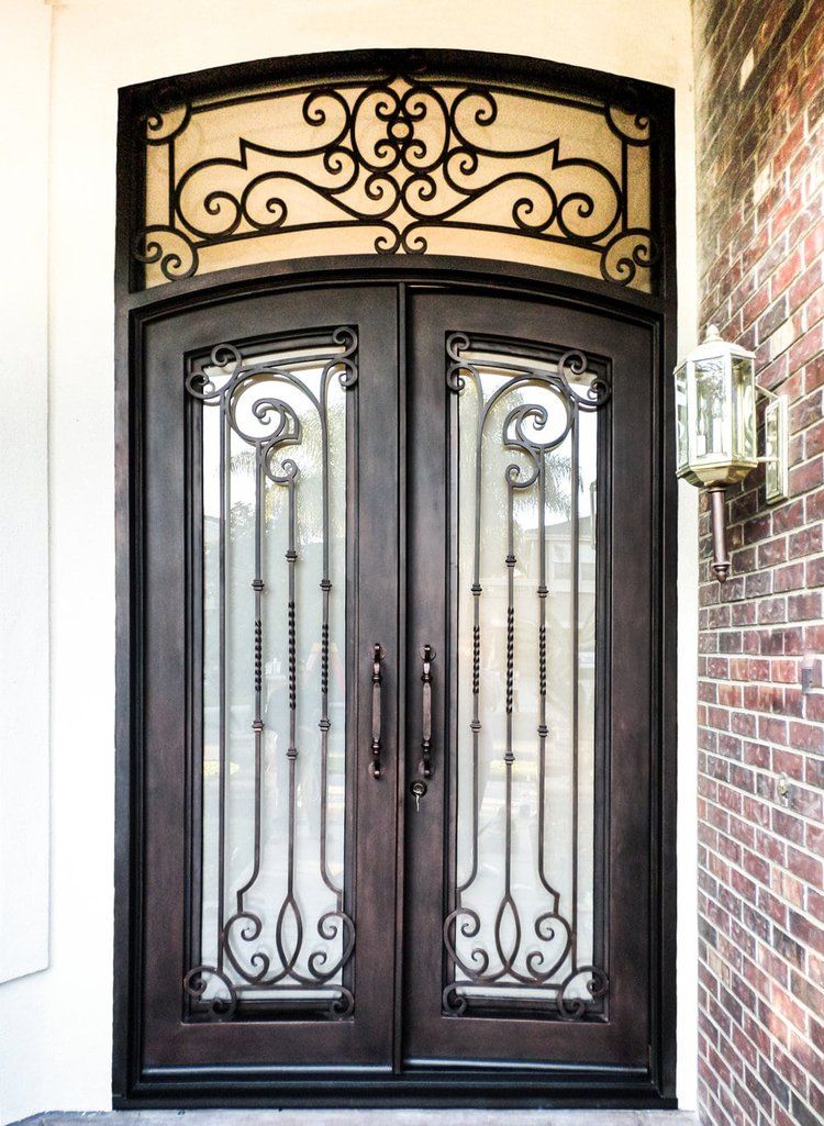 A wrought iron door with a brick wall behind it.