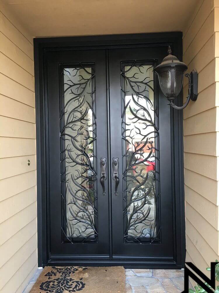 A black door with a wrought iron design and a lamp on the side of a house.