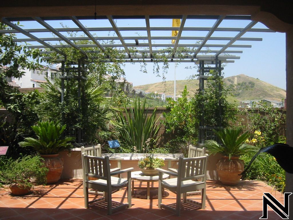 A patio with a table and chairs under a pergola with the letter n in the corner