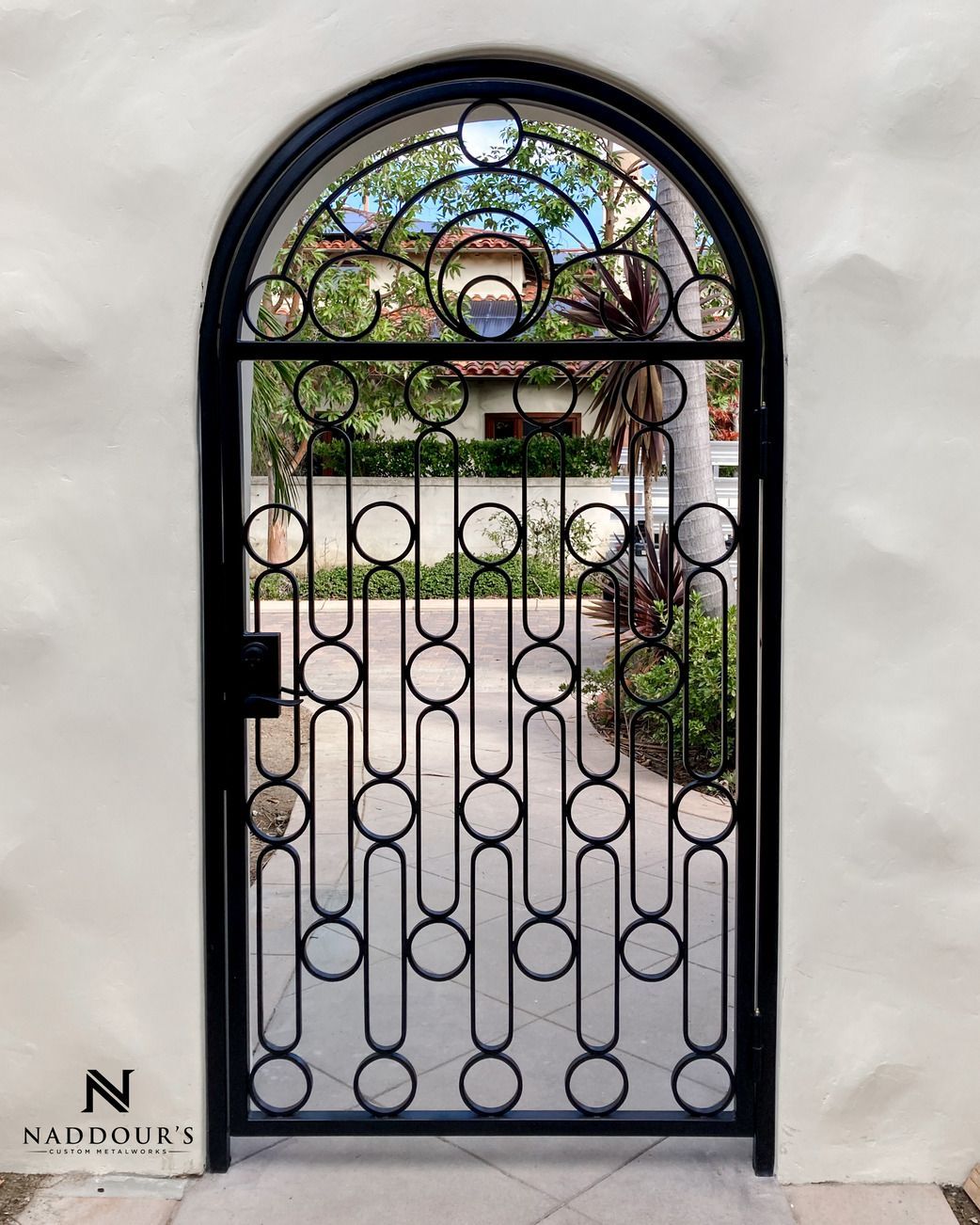 A wrought iron gate with circles on it is sitting on a sidewalk in front of a white wall.