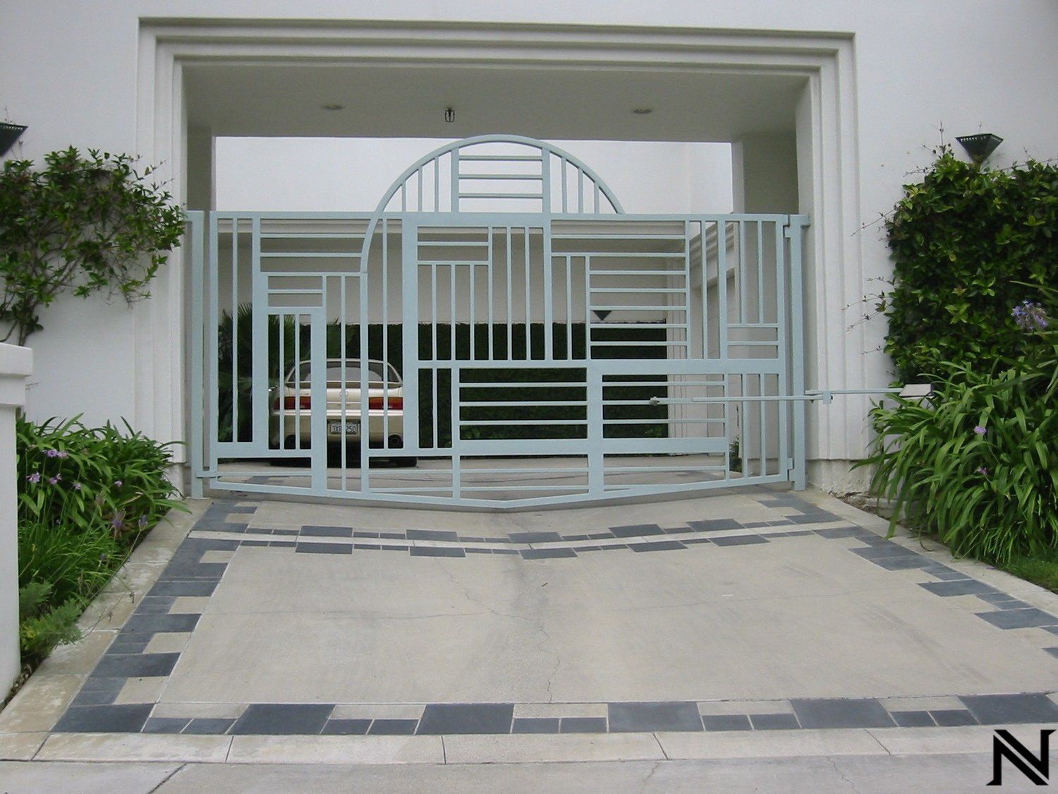 A car is parked in a driveway behind a gate that says n on it