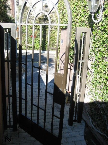 A wrought iron gate is open to a brick walkway