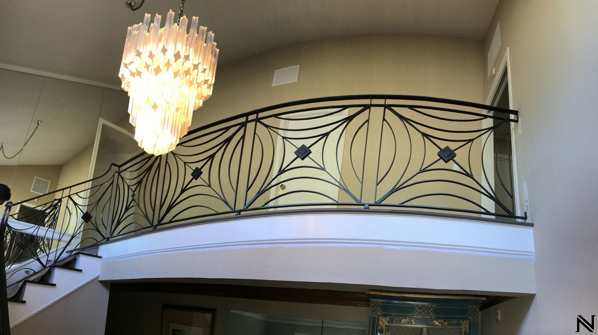 A staircase with a wrought iron railing and a chandelier hanging from the ceiling.