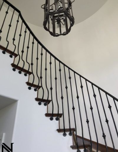 A curved staircase with a wrought iron railing and a chandelier hanging from the ceiling