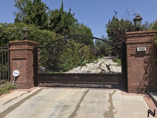 A wrought iron gate is surrounded by brick pillars and trees.