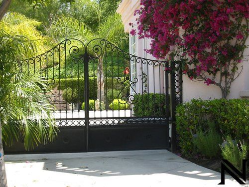 A black wrought iron gate with purple flowers in the background