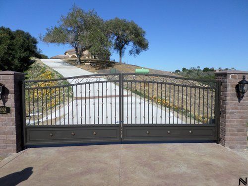 A black gate is open to a driveway with a house in the background
