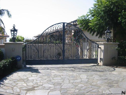 A stone driveway with a wrought iron gate leading to a house