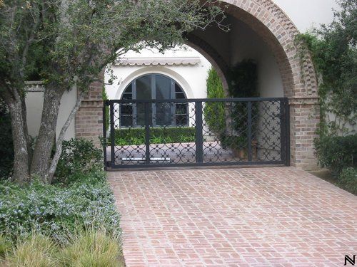 A brick archway with a black gate leading to a house