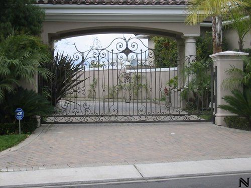 A driveway with a wrought iron gate leading to a house