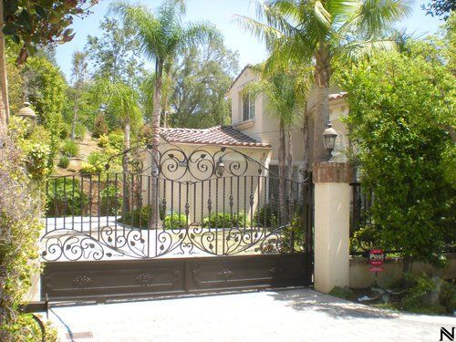 A wrought iron gate leading to a house with a palm tree in the background