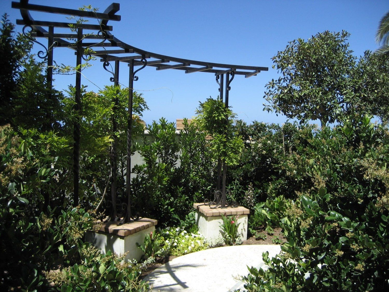 A pergola is surrounded by trees and bushes on a sunny day